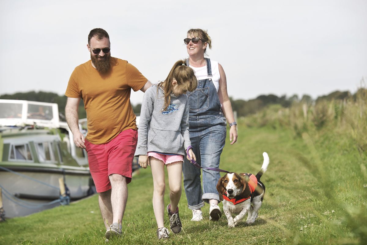 Family and a dog walking on a grassy bank at Acle Bridge moorings