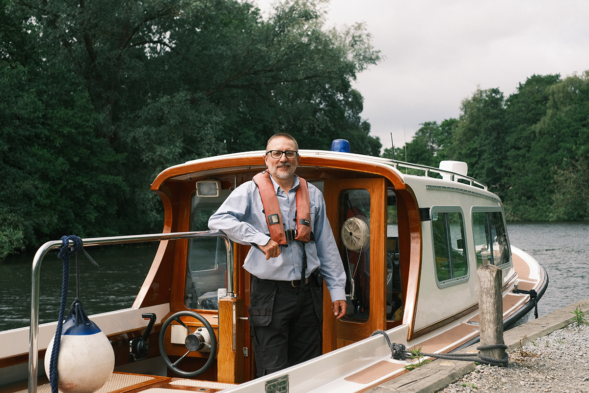 We employ a combination of field-based staff, such as our Rangers and Op Techs, and office-based teams such as Planning, Communications and Governance A person wearing a life jacket stands on the deck of a traditional cabin cruiser moored along a peaceful waterway. Surrounded by mature trees and calm river water, the scene captures recreational boating in the tranquil setting of the Broads.