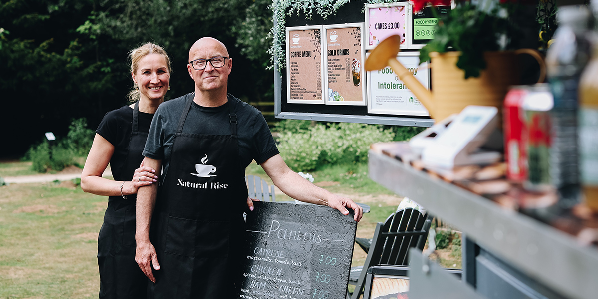 Two Natural Rise team members standing beside their outdoor food trailer at How Hill.