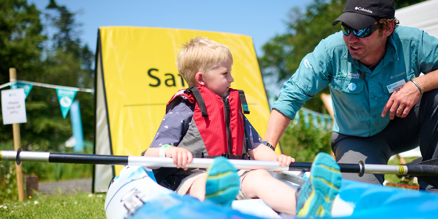 BA_RNS796.jpg An outdoor nature activity where a guide shows two children aquatic wildlife in a clear water tray under a marquee, with event tents and banners in the background.