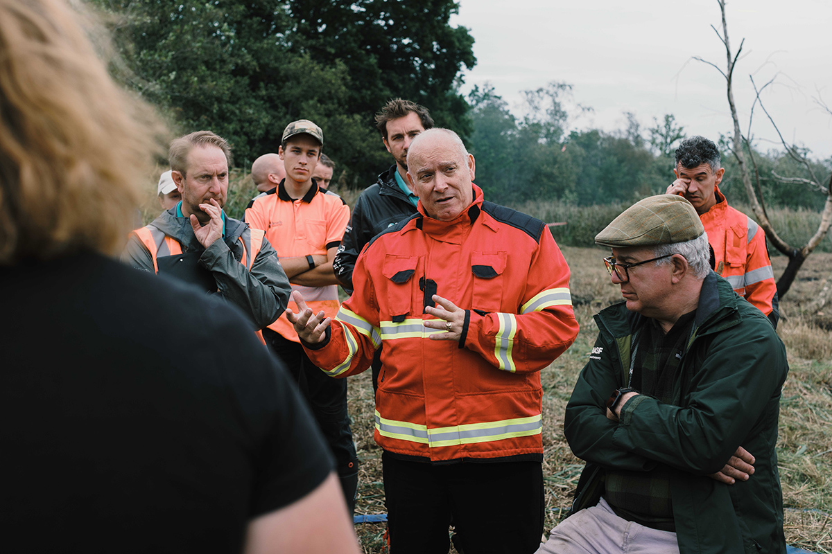 Ray Harcourt, Watch Commander and Wildfire Lead for Norfolk Fire Service A group of people gathered outdoors at a wildfire awareness event, with a man in an orange emergency-services uniform speaking to the group.